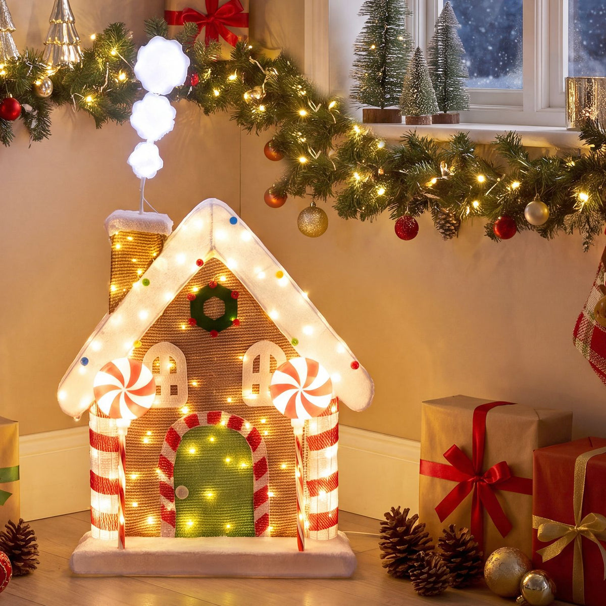 Front-facing view of the glowing gingerbread house beneath a decorated garland, with wrapped gifts nearby.