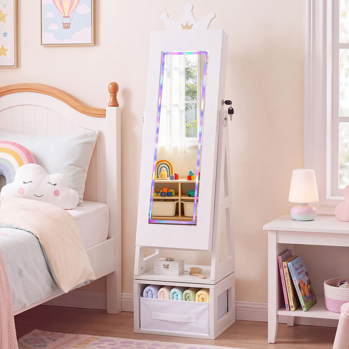 White crown-shaped jewelry cabinet with an illuminated mirror beside a child’s bed and bedside table.