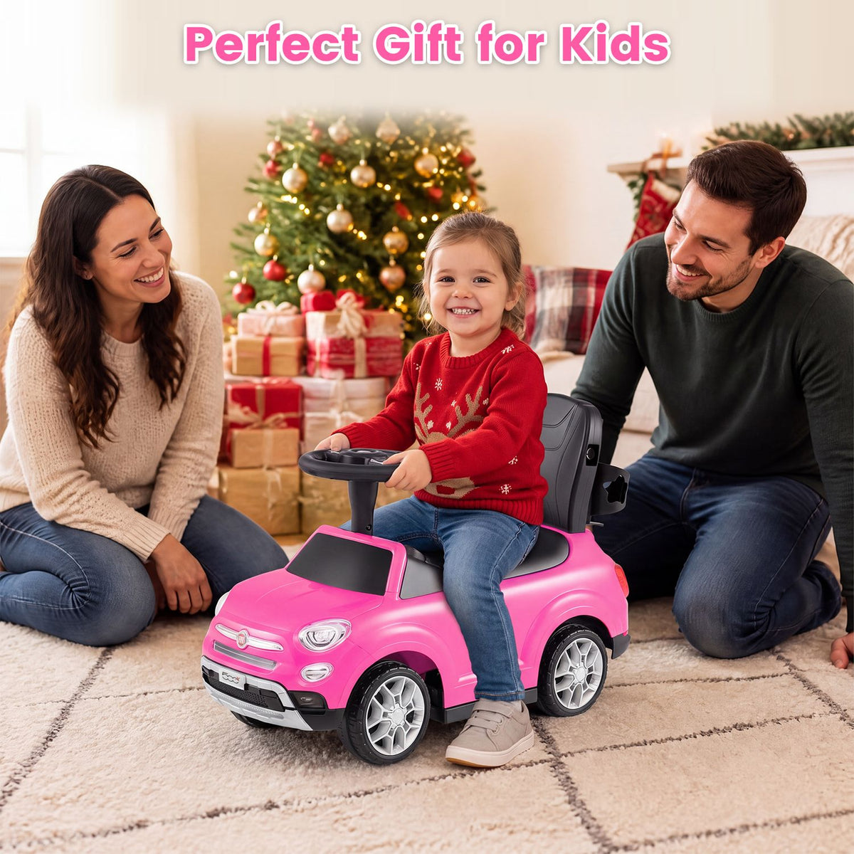 A child sits on a pink ride-on car between two adults in a festive living room.
