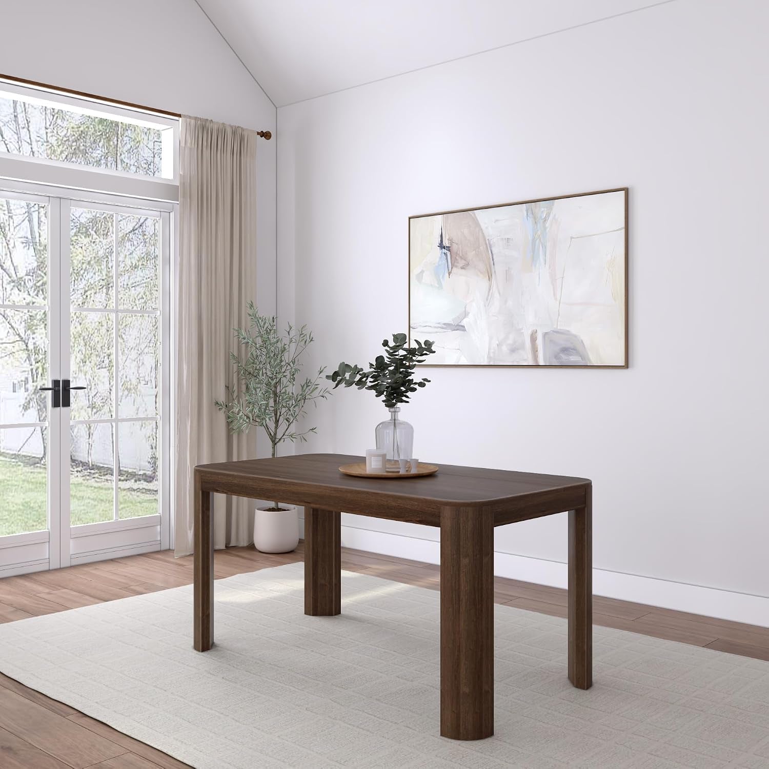 Full room view of a walnut dining table centered on a light rug with a vase and wall art.