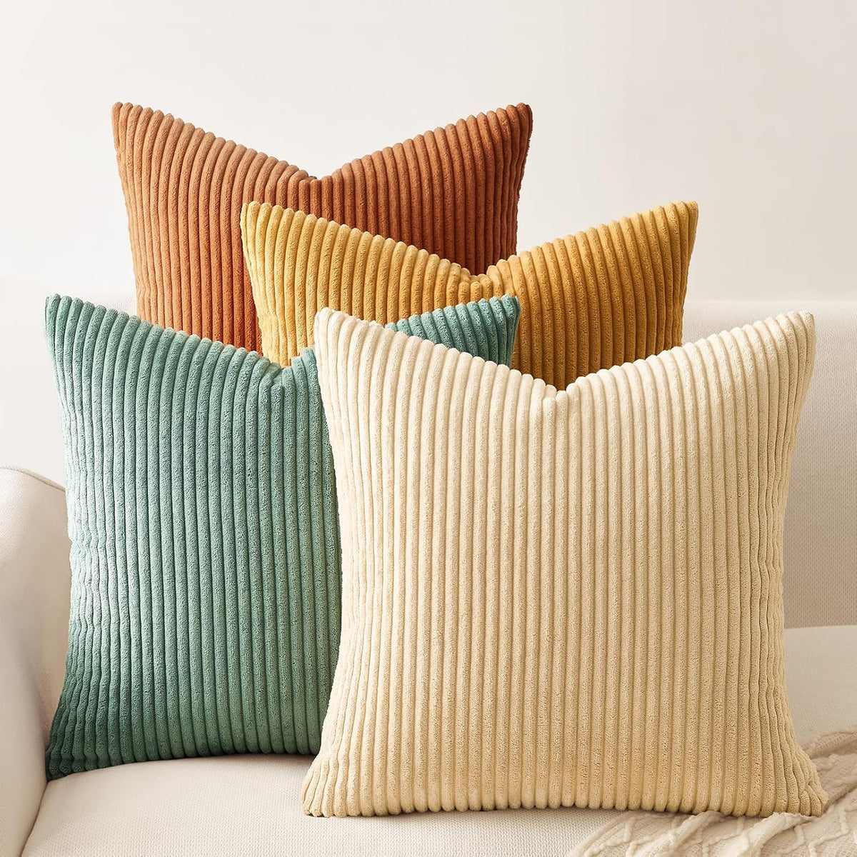 Close front view of four ribbed corduroy pillows (cream, teal, mustard, rust) arranged on a light sofa.