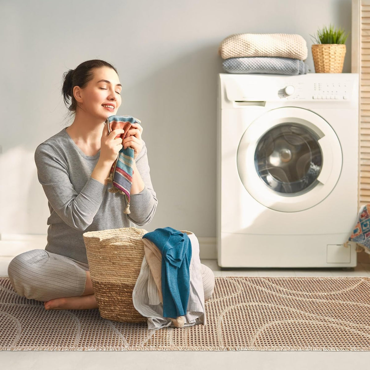 Woman folding laundry while sitting on a long beige woven mat in front of a washing machine