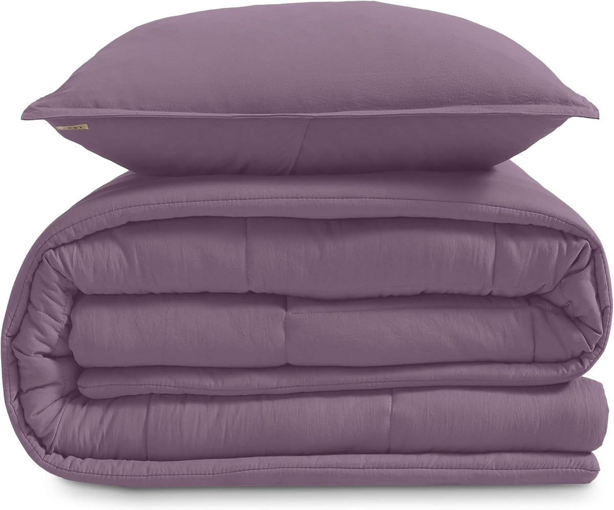 Stacked folded comforter and a single sham in muted lavender shown from the front on a white background.