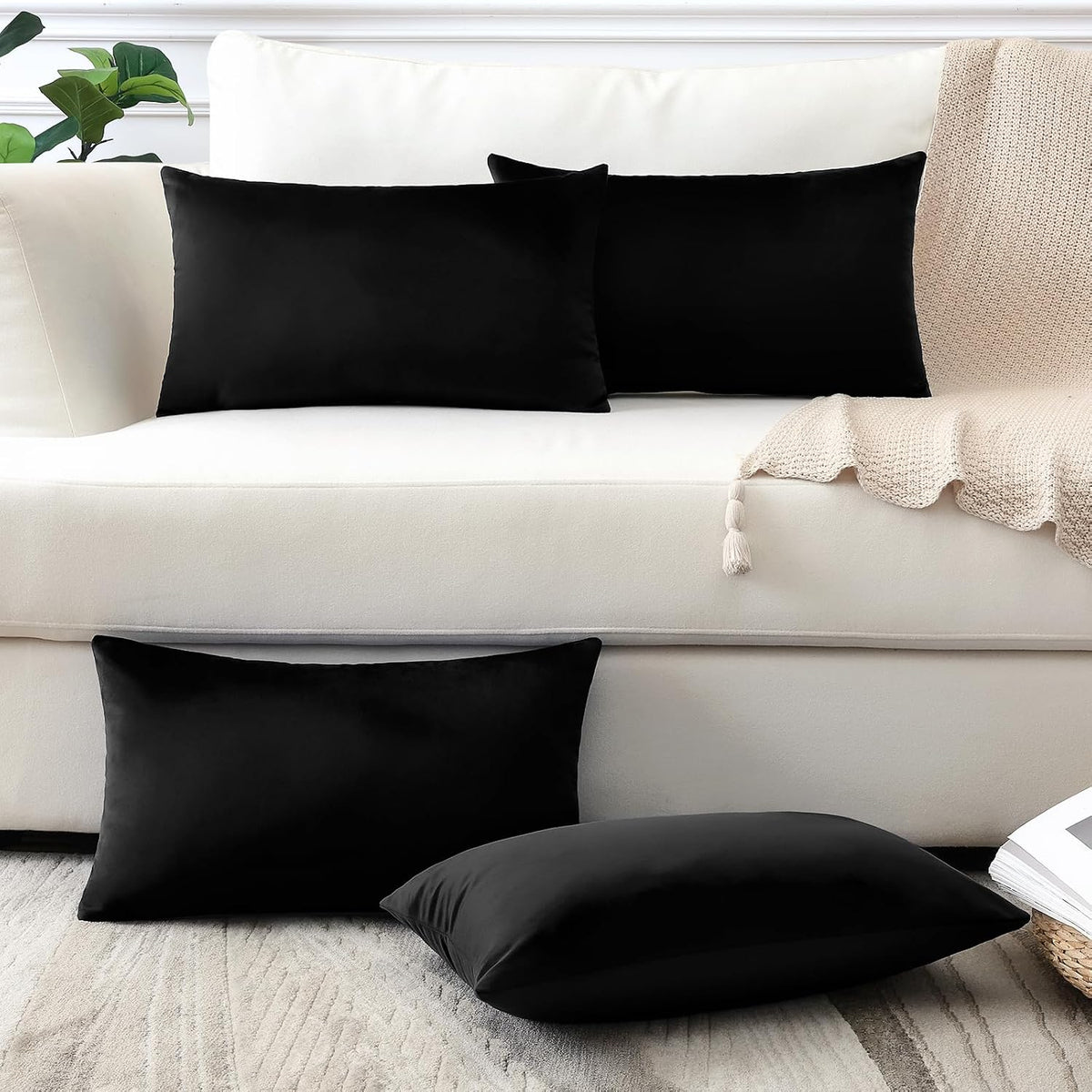 Two rectangular and two square black pillow covers styled on a white sofa and floor