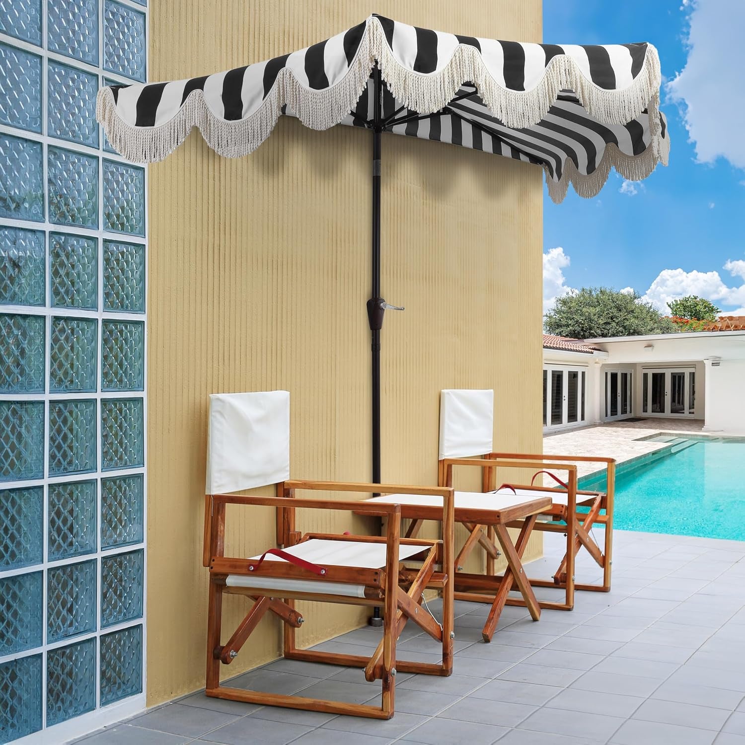 Striped half umbrella mounted on dark brown pole beside a pool with two wooden chairs on a patio.