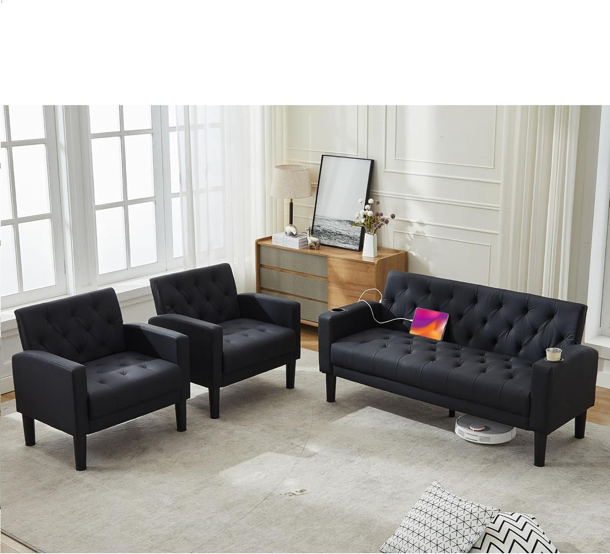 Black loveseat and two matching armchairs with a tablet plugged in and a robot vacuum parked under the sofa.