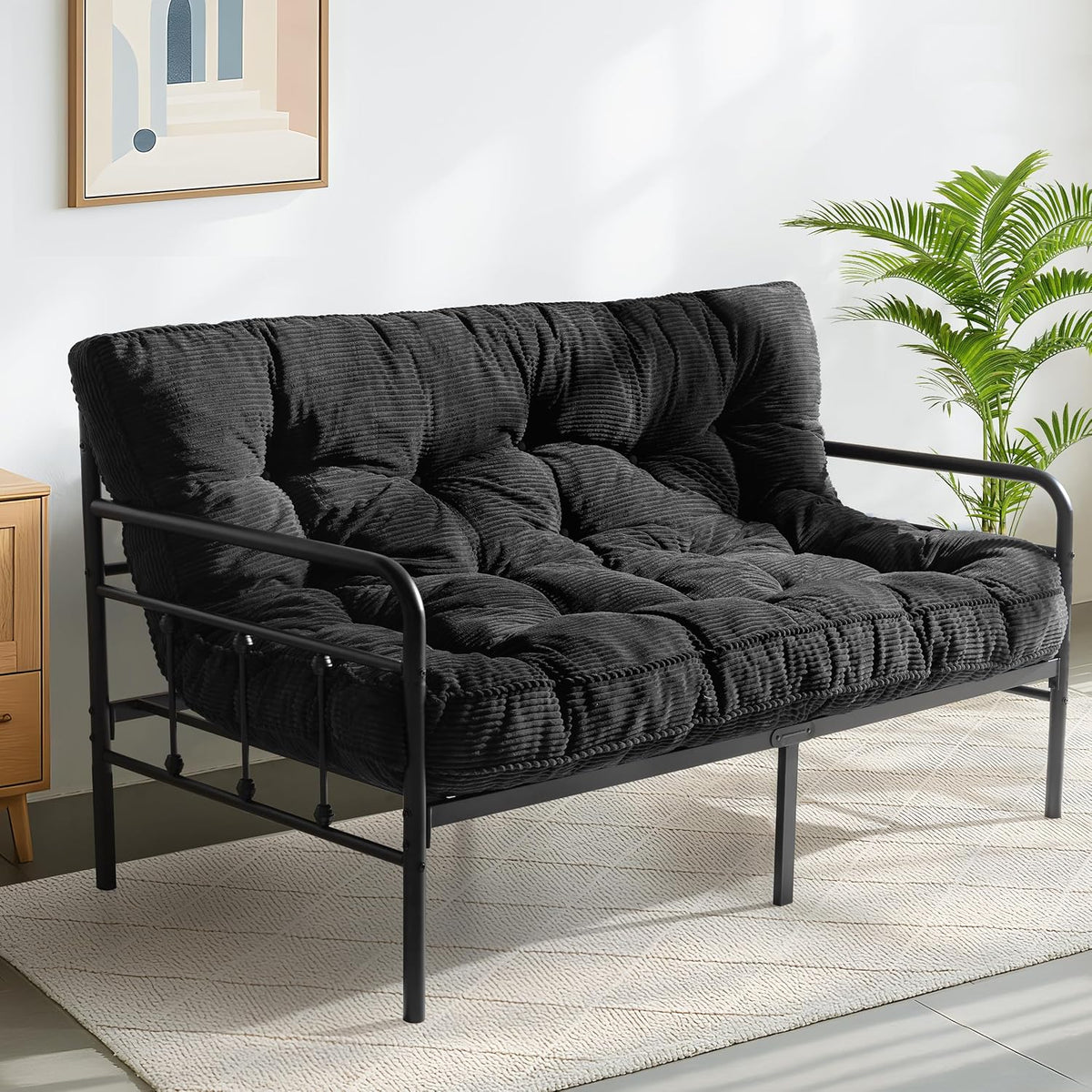 Front three-quarter view of a black tufted futon mattress on a black metal frame with sunlight on the rug.
