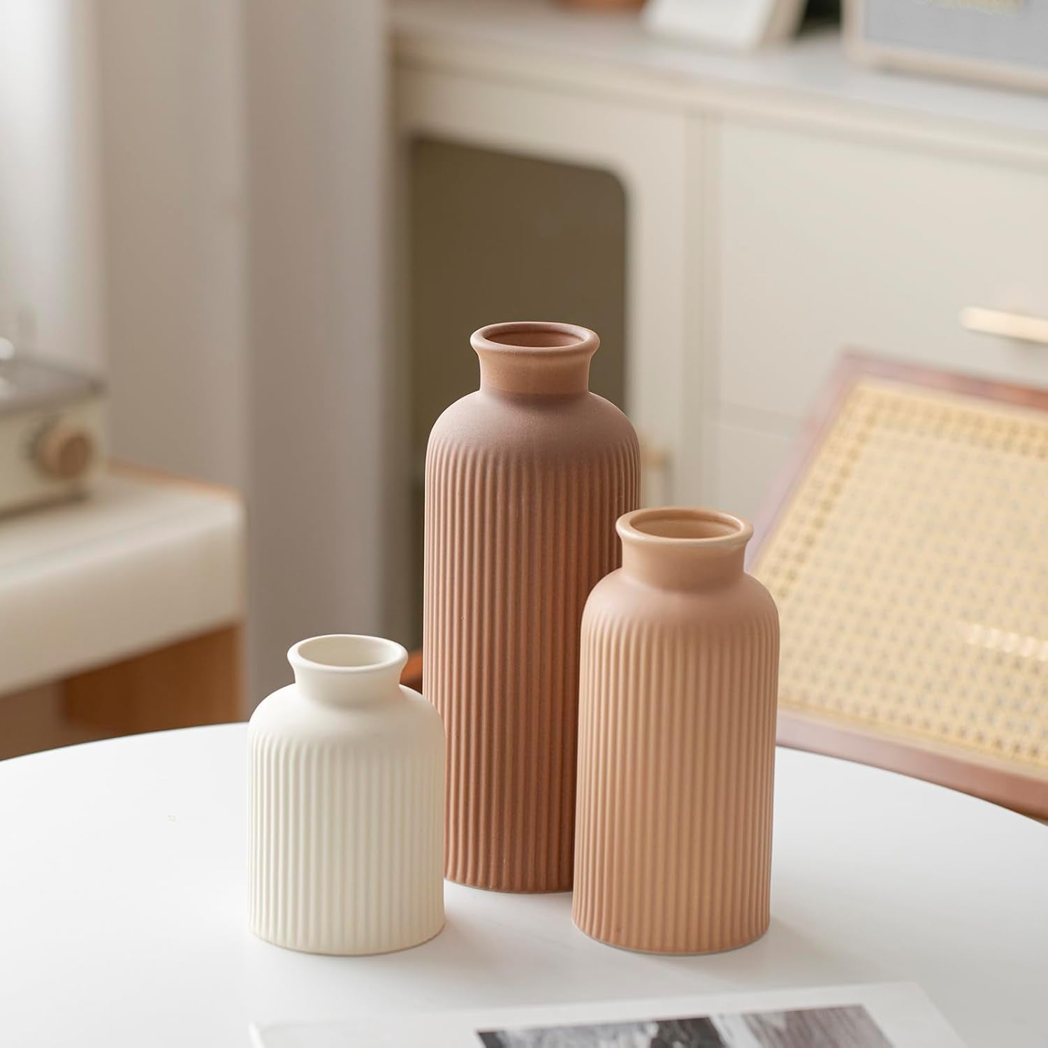 Three ribbed ceramic vases in cream, light terracotta and brown grouped on a white surface, angled studio shot.