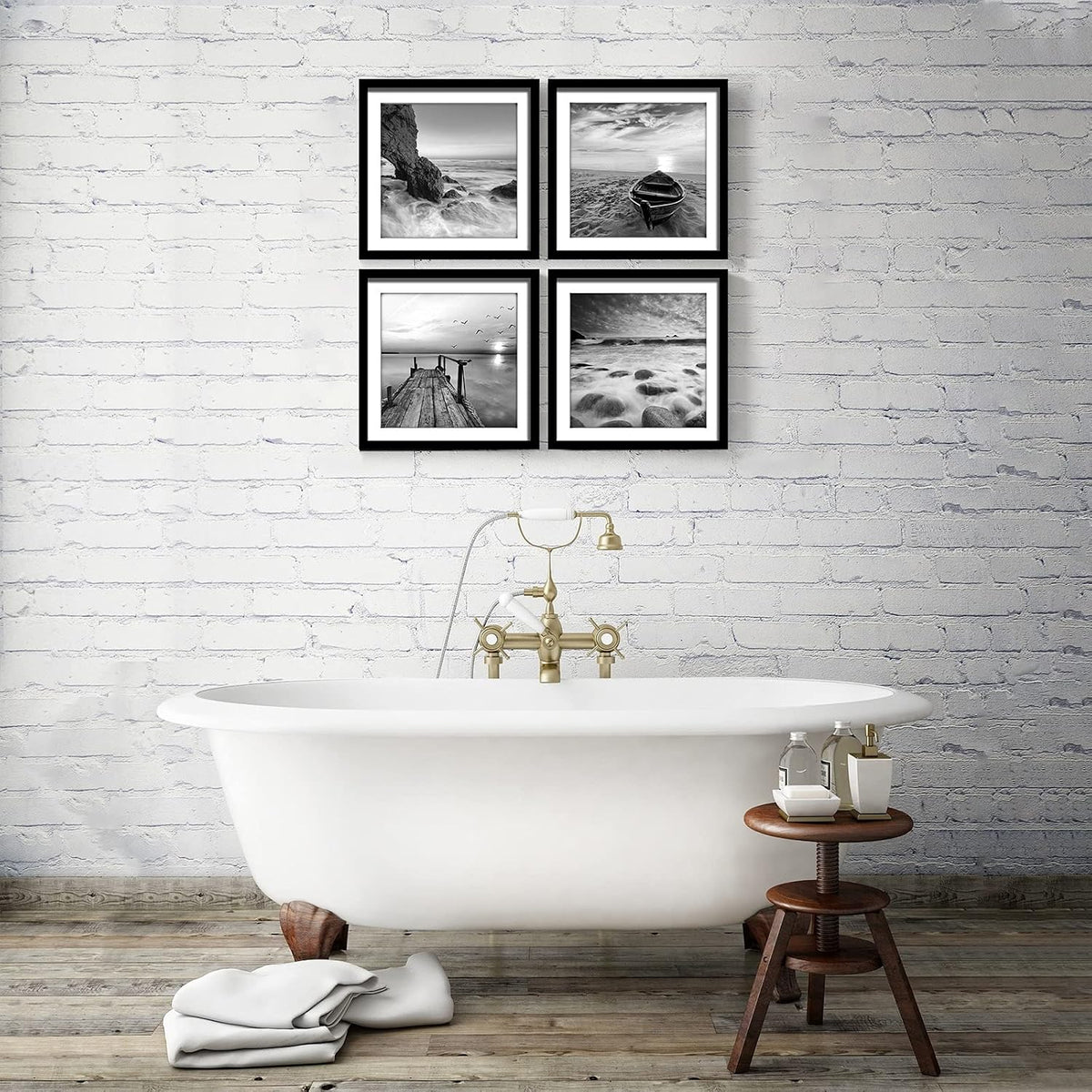Four black-and-white seascape framed prints arranged 2x2 above a freestanding bathtub against a white brick wall