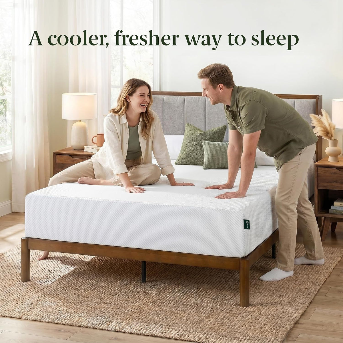 Couple smiling and leaning on a white mattress set on a wooden bed frame in a bright bedroom