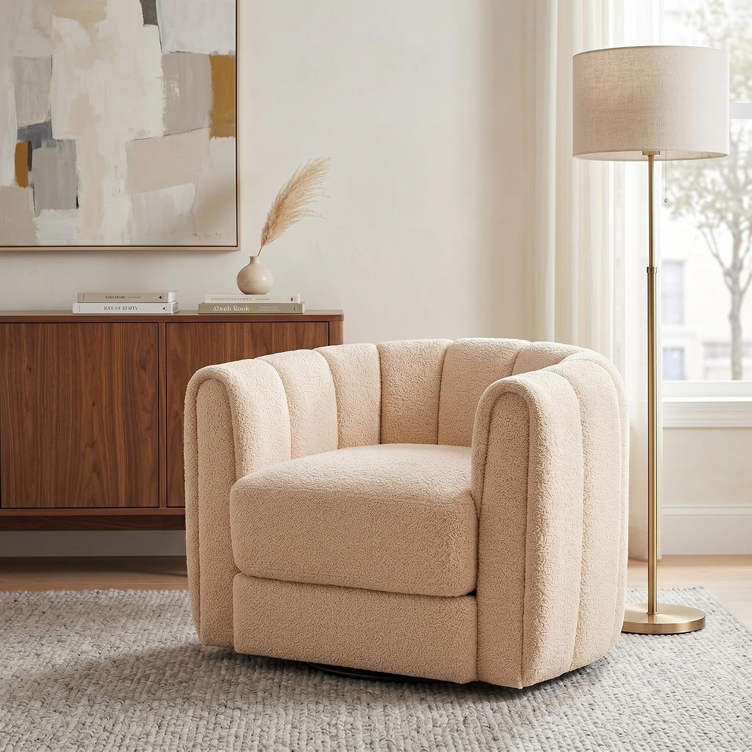 Cream-colored round barrel swivel chair beside a wooden credenza and floor lamp in a neutral room.