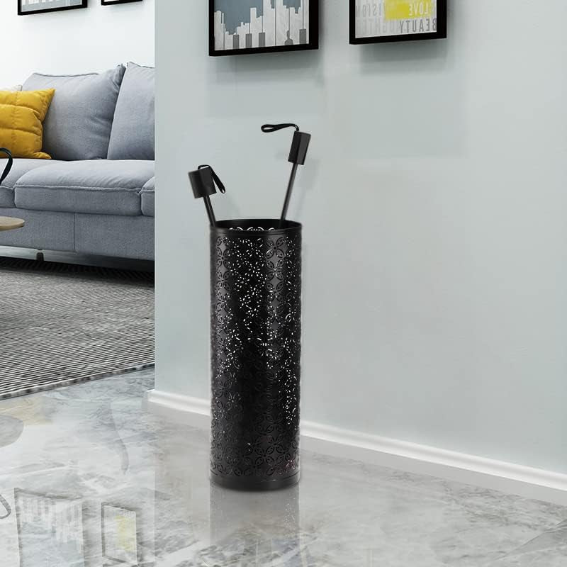 Black cylindrical metal umbrella stand with decorative cutouts placed against a white wall, holding two umbrellas.