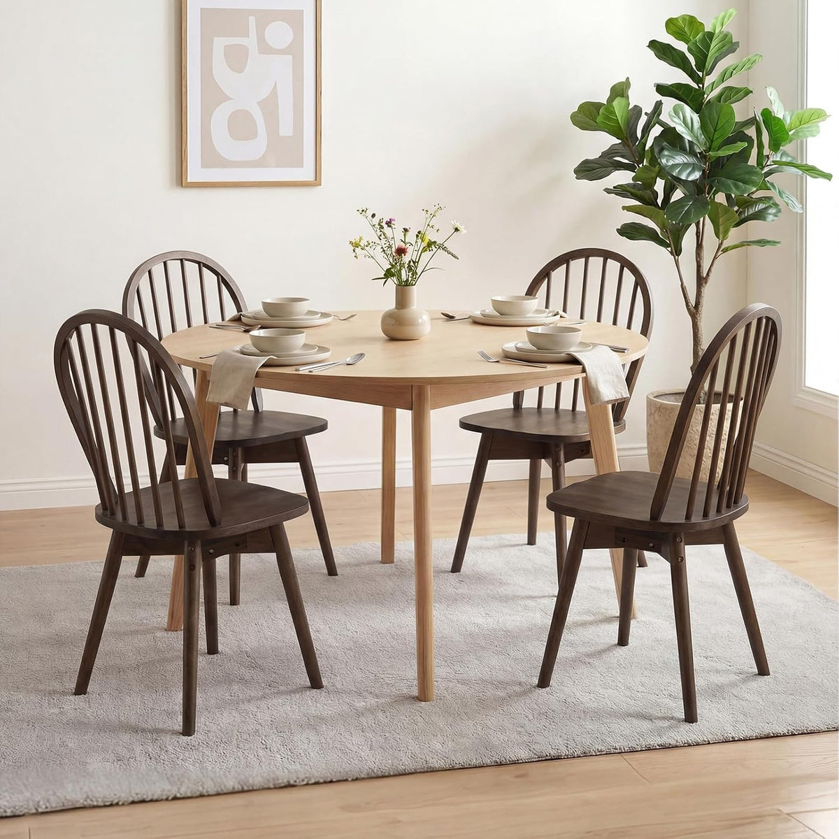 Four walnut Windsor chairs arranged around a round light-wood dining table in a bright dining room