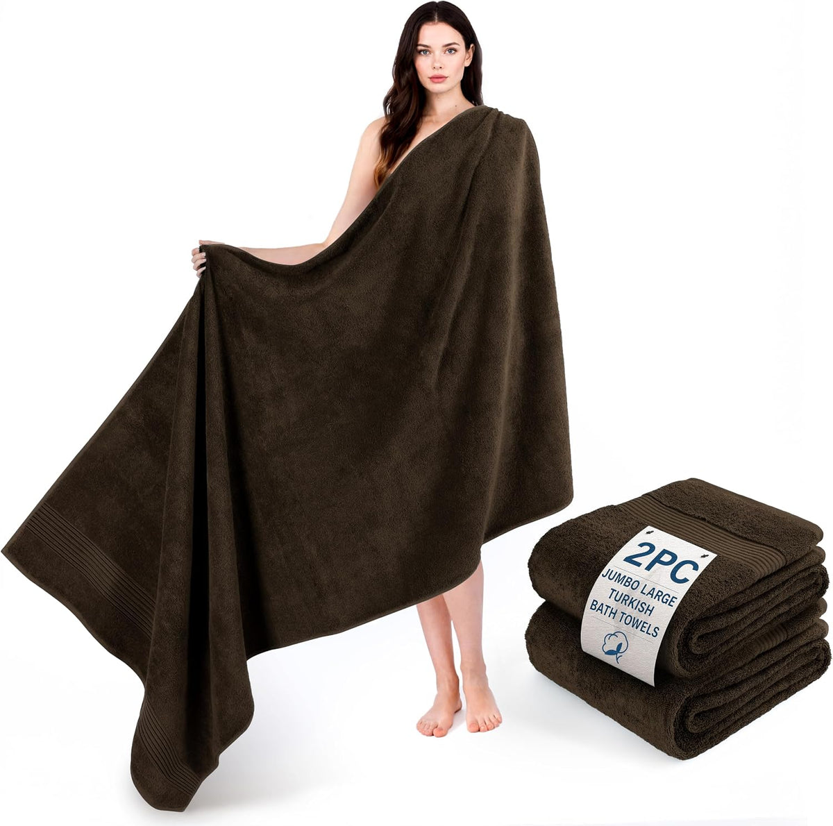 Woman holding open a large dark brown bath towel with a matching folded pair placed on the floor nearby