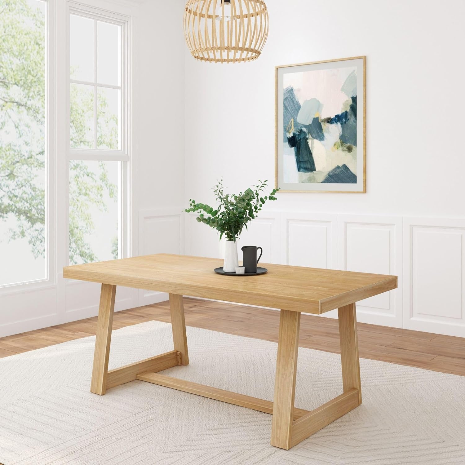 Angled view of a pecan dining table with a small tray and vase on top in a bright room.