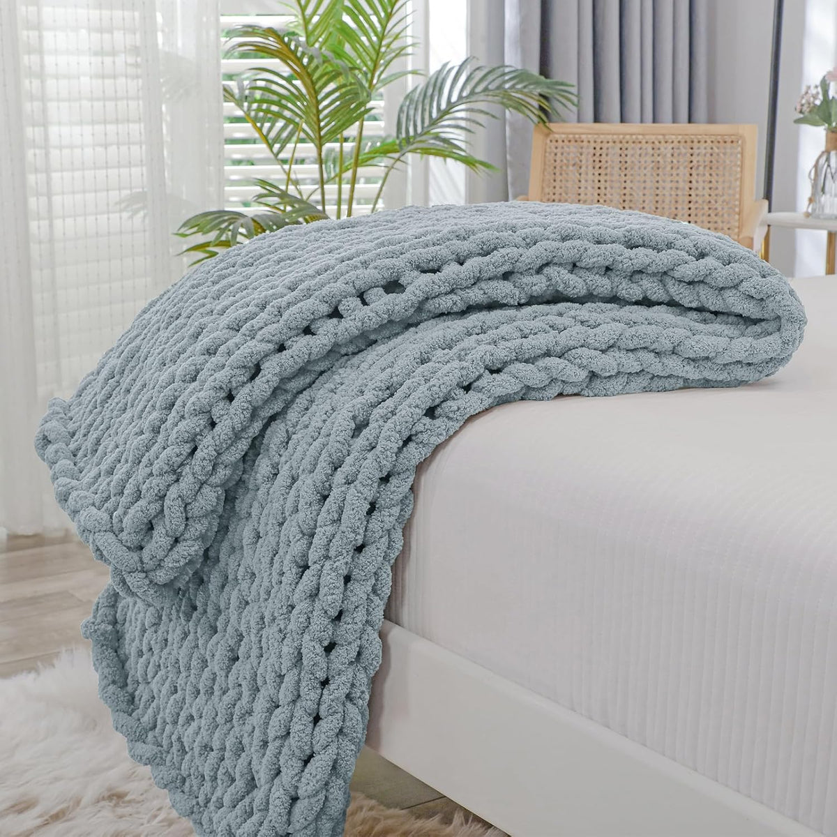 Light blue chunky knit throw neatly folded and laid across the end of a white bed.
