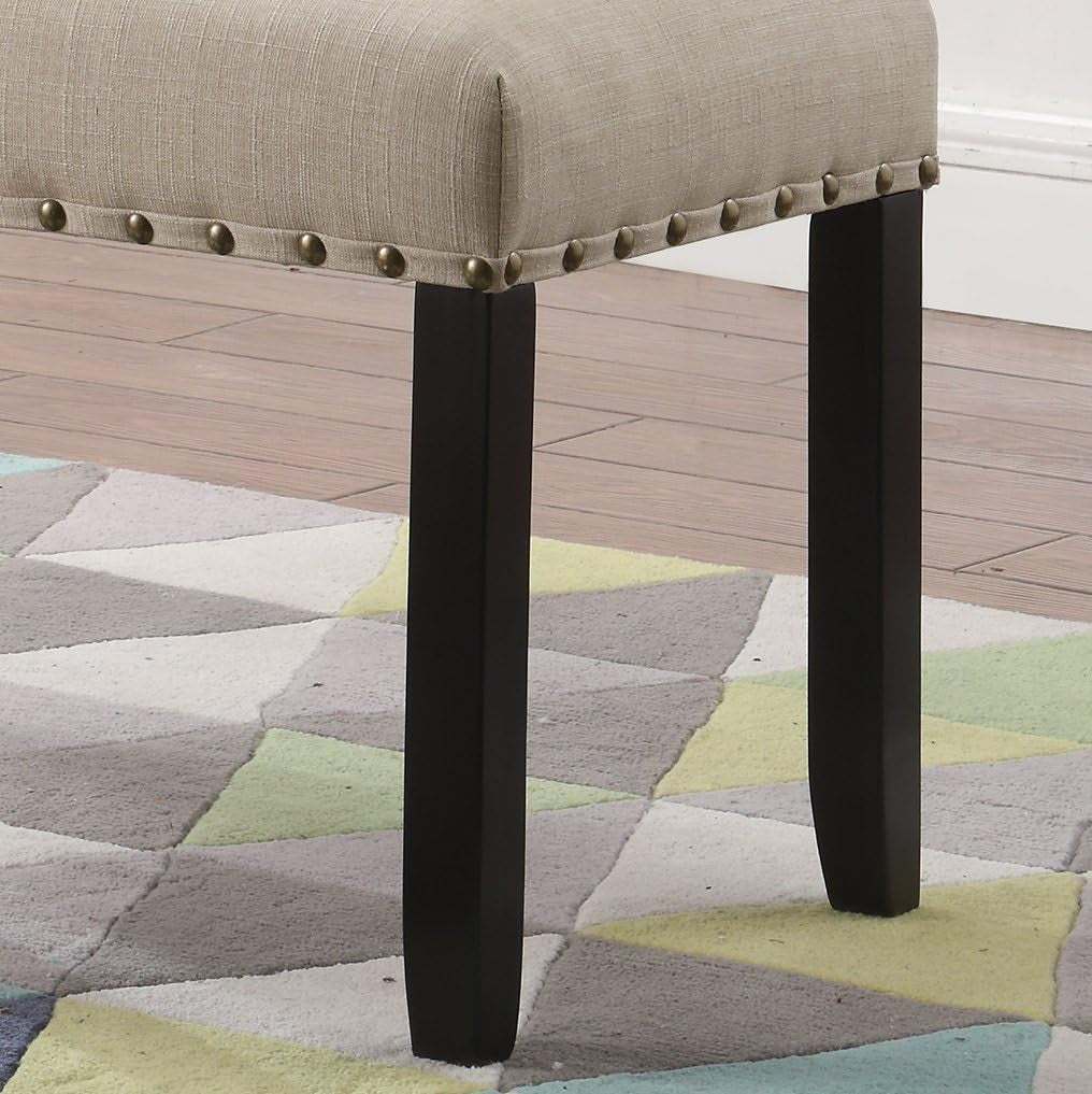 Close-up of black hardwood leg and tan fabric seat with brass nailhead trim on a patterned rug