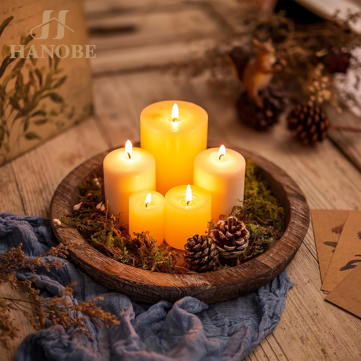 Round rustic wooden tray holding five lit pillar candles with moss and pinecones, styled on a wooden surface