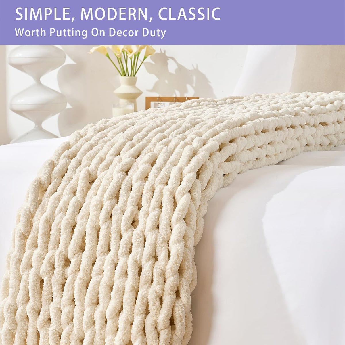 Close-up of a beige chunky knit throw draped over a white bed, showing thick braided rows.