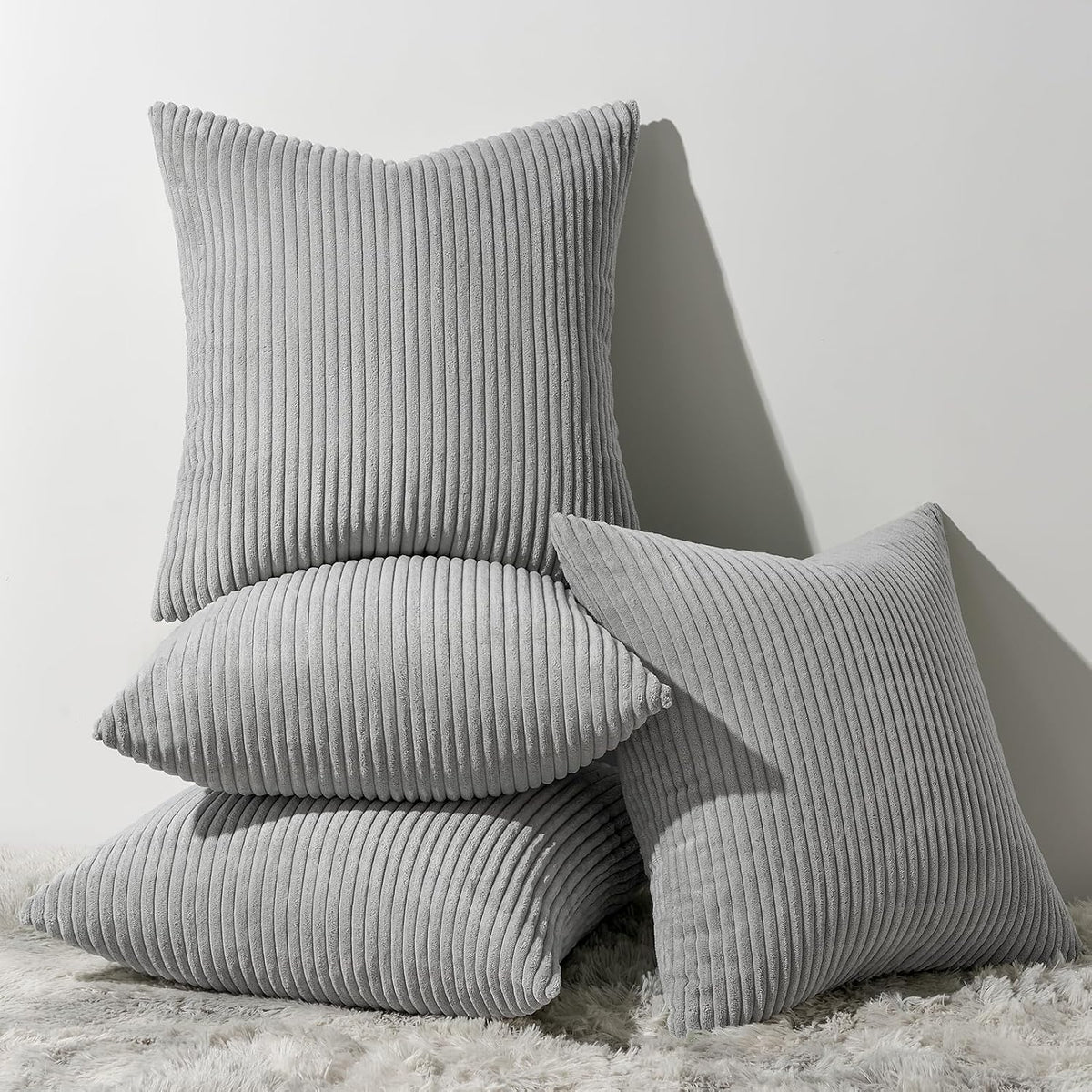 Pile of grey ribbed corduroy square pillows arranged on a shaggy rug with shadowed wall