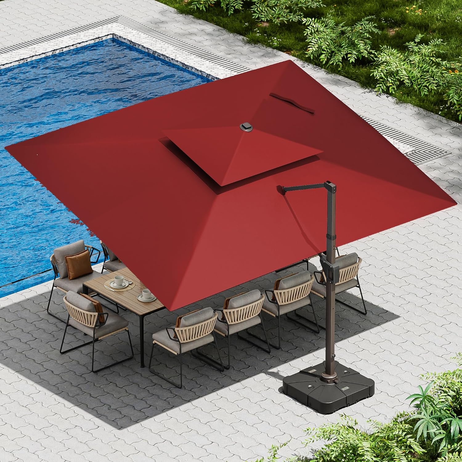 Aerial view of a red square cantilever umbrella shading a long dining table beside a pool.