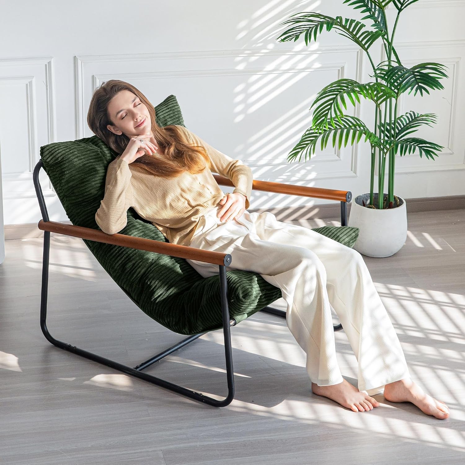 Lifestyle image of a person reclining on the dark green corded-fabric accent chair in a bright room