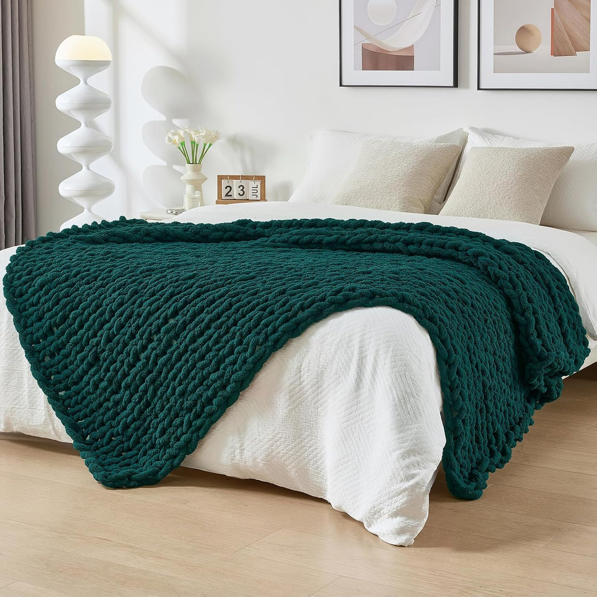 Deep green chunky knit throw unfolded across the foot of a made bed in a bright bedroom.