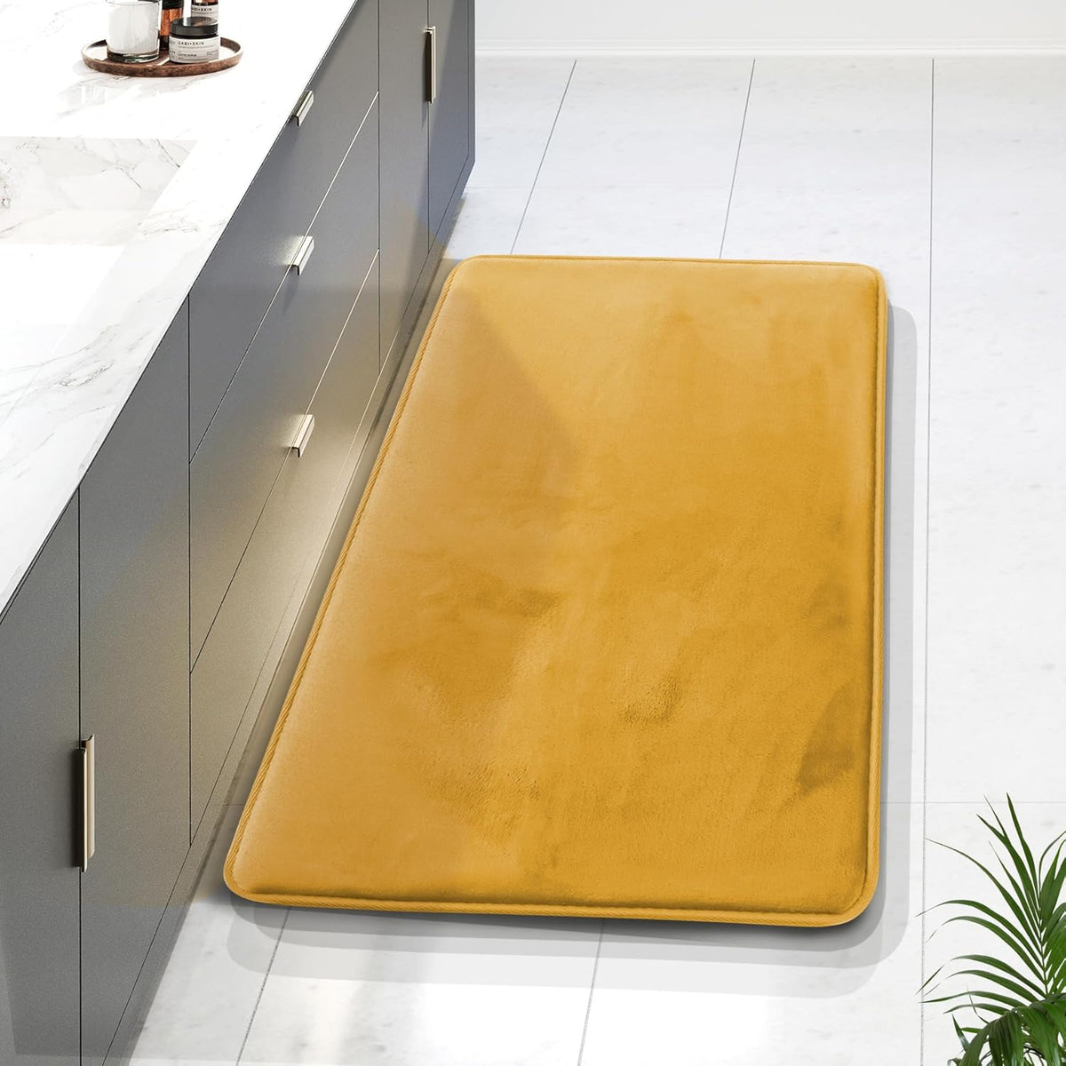 Angled view of a mustard-yellow long runner placed beside gray cabinets on a white tiled floor in a kitchen-style setting.