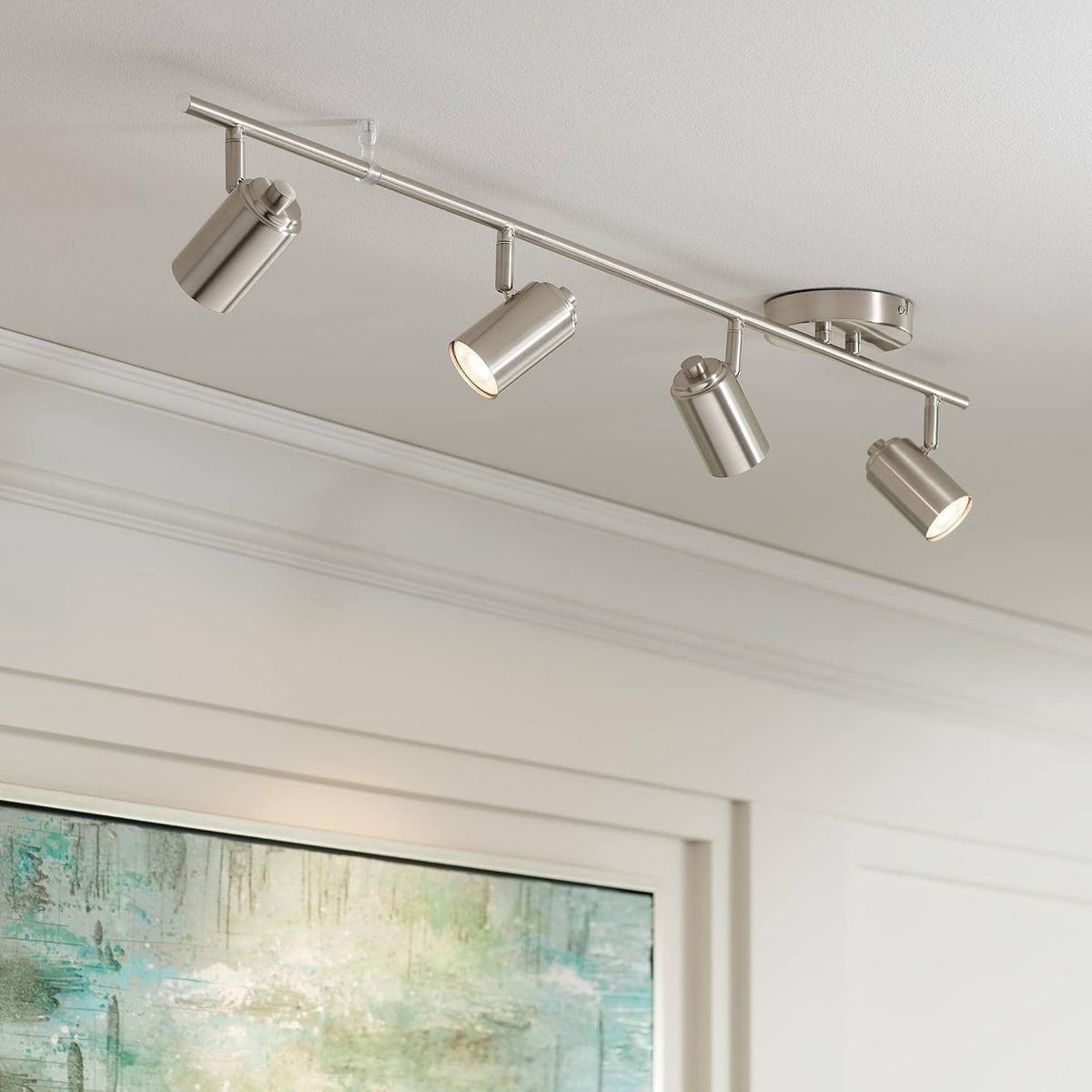 Brushed nickel 4-light track fixture installed on a white ceiling angled view over framed artwork