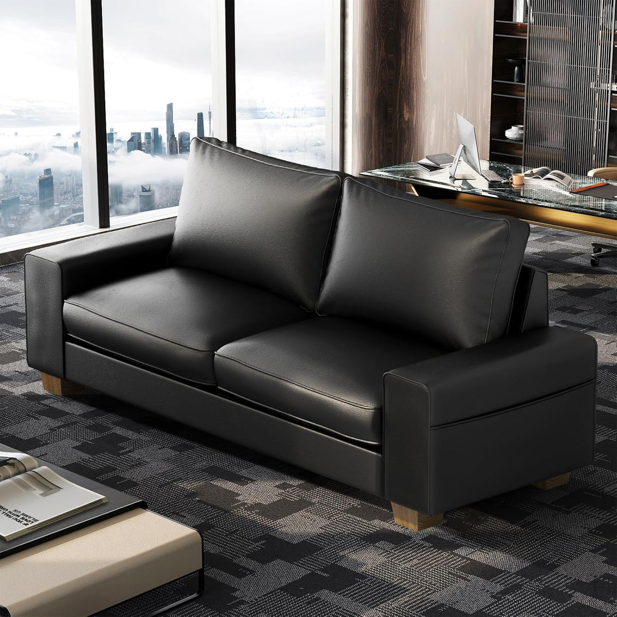 Angled view of a black faux-leather loveseat in a high-rise office with large windows and city skyline