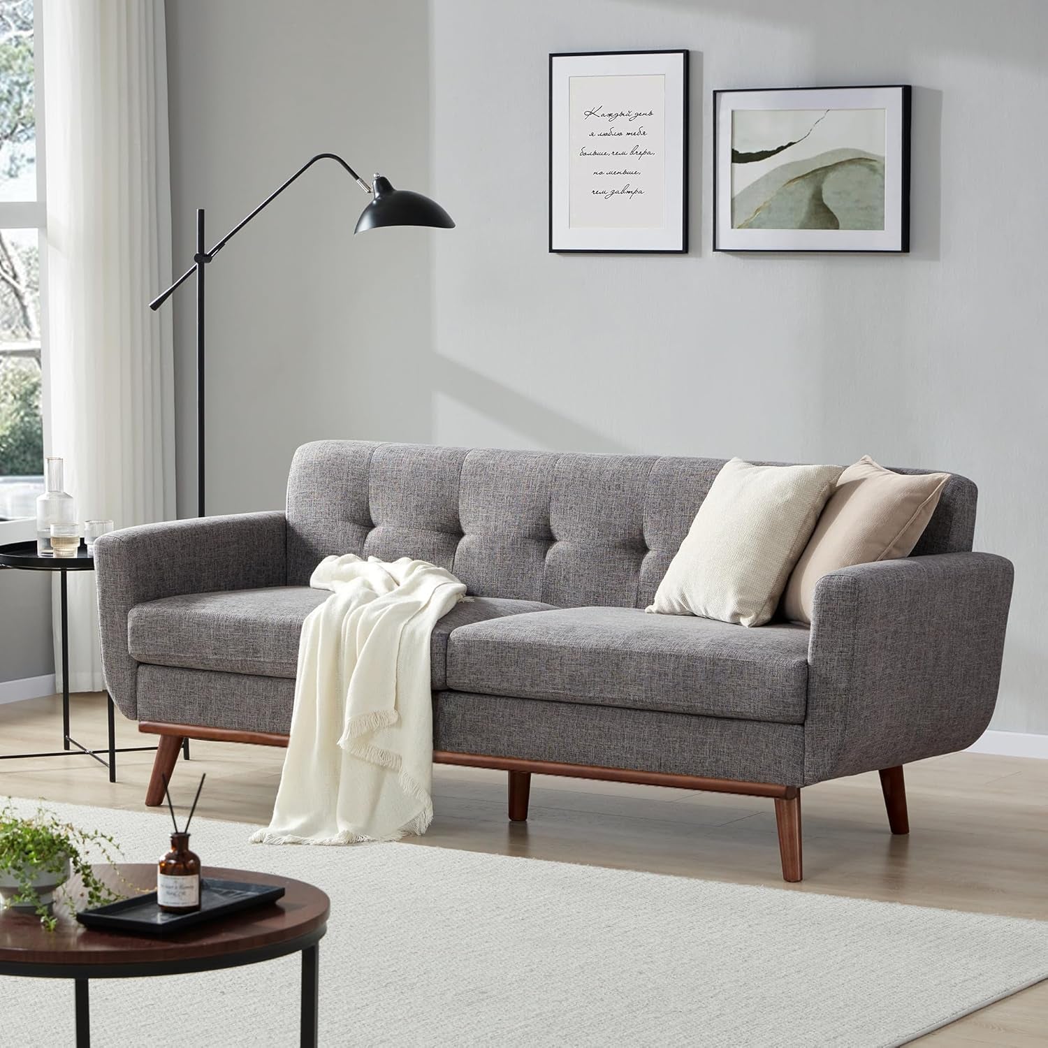 Gray tufted three-seat sofa with throw and pillows against a light wall