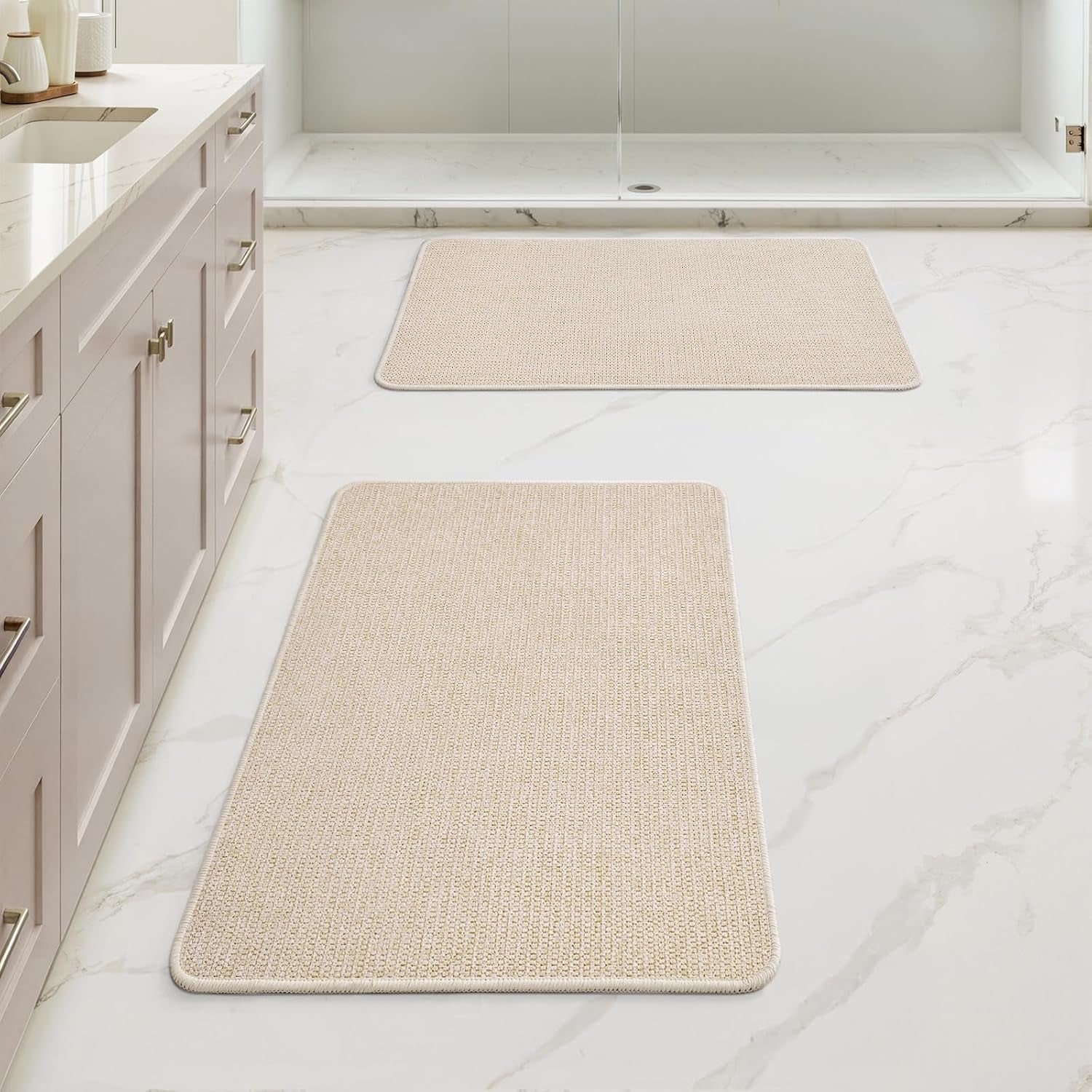 Bathroom floor with two light cream rugs shown in front of a shower and sink cabinet.