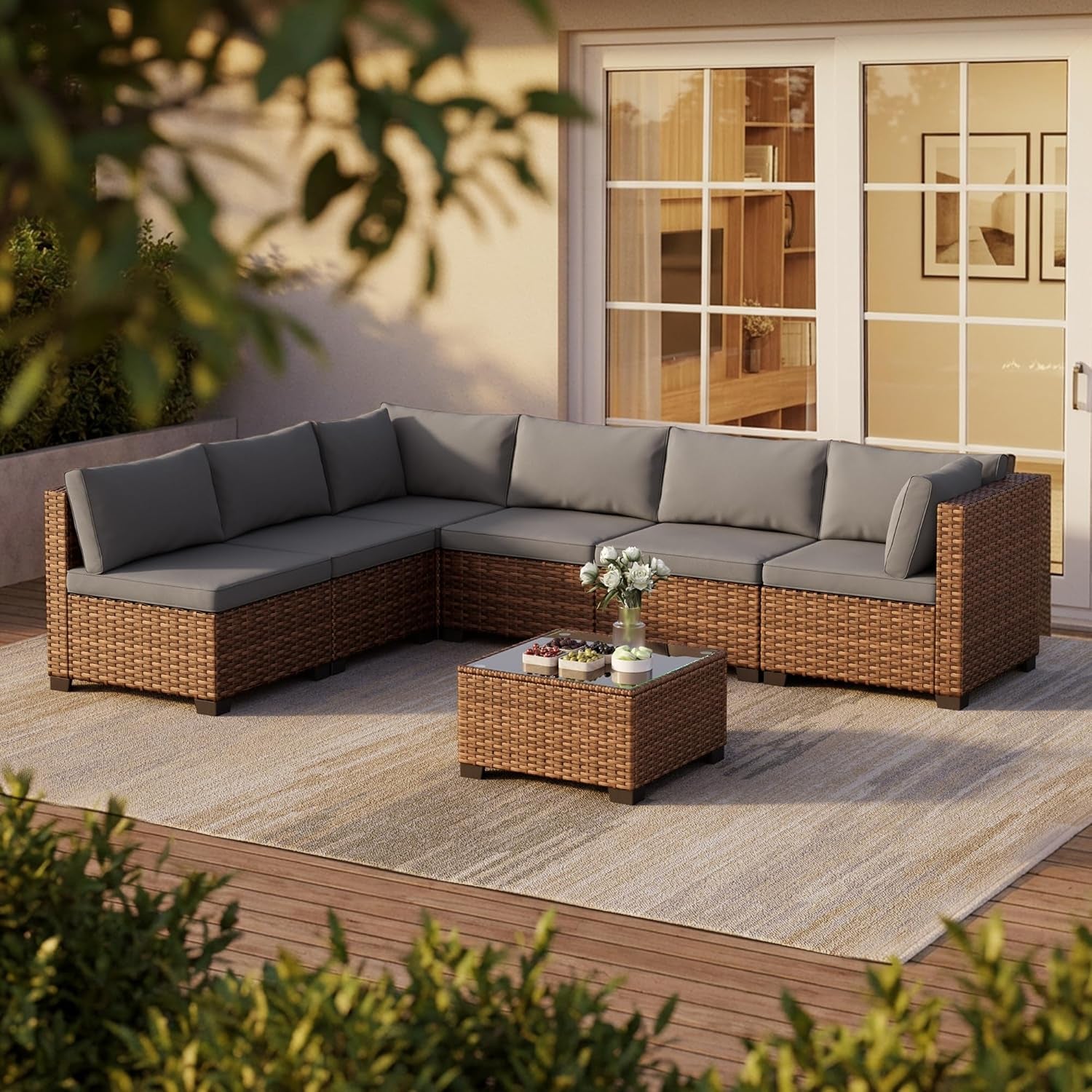 Brown PE rattan sectional with grey cushions and tempered glass coffee table on a deck, angled front view