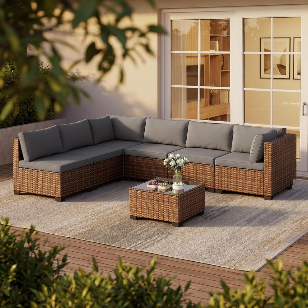Brown PE rattan sectional with grey cushions and tempered glass coffee table on a deck, angled front view