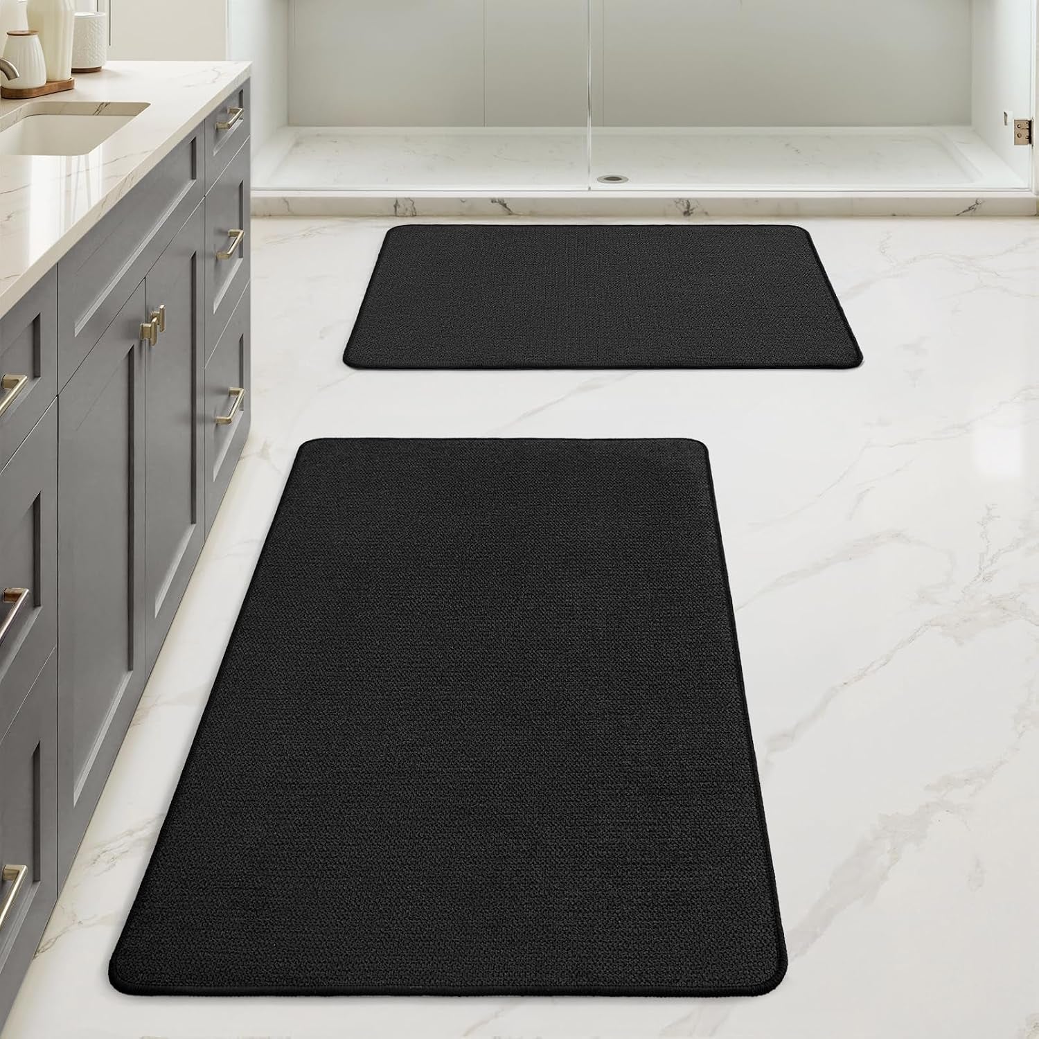 Floor-level perspective showing two black rectangular bath mats aligned along a vanity and shower.
