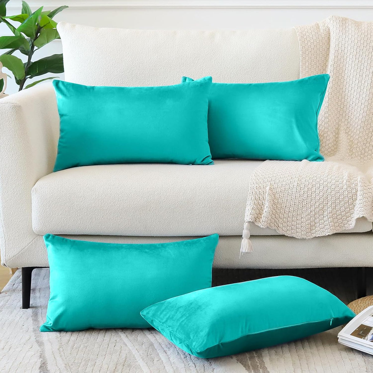 Two rectangular and two square teal throw pillow covers arranged on a cream sofa and rug.
