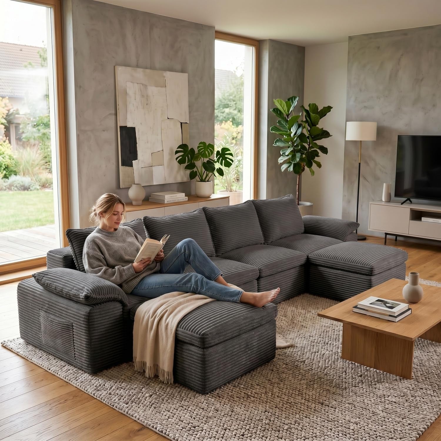 Dark gray corduroy sectional with chaise and ottoman in a modern living room; woman reading on the sofa.