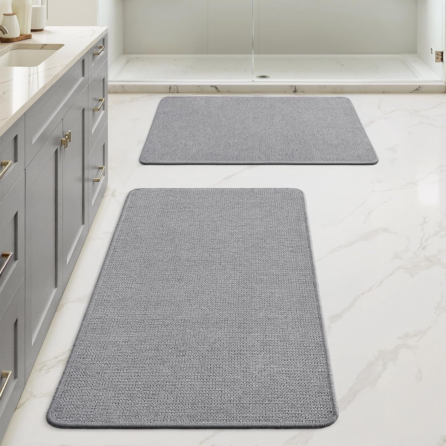 Pair of light gray rectangular rugs placed down the bathroom floor beside a gray vanity and shower