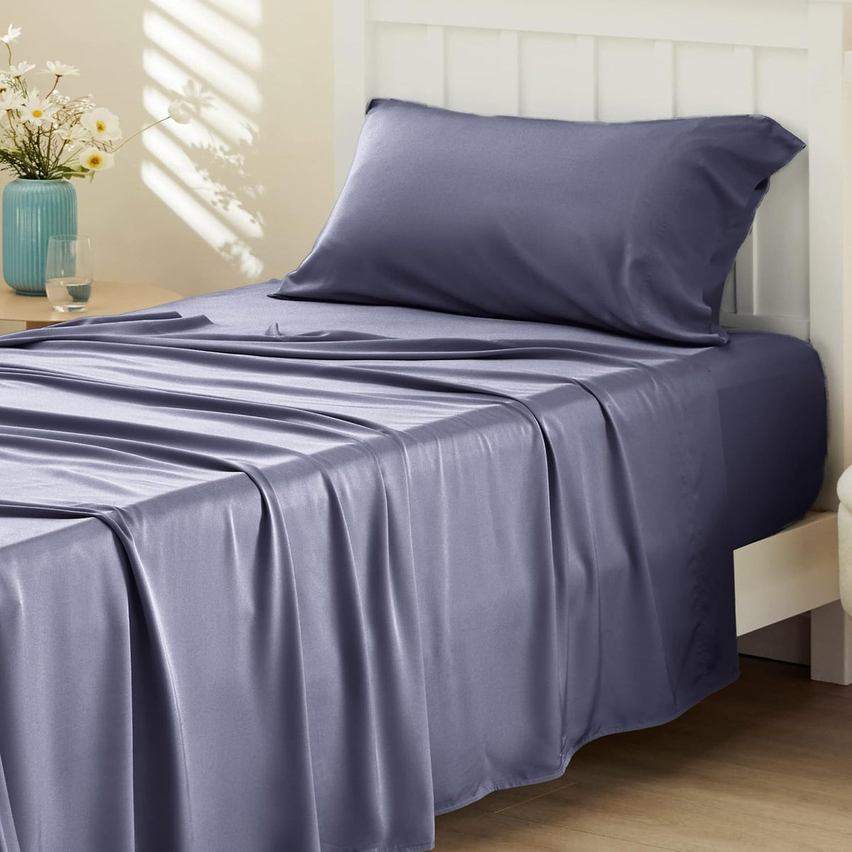 detail — close-up of a slate-lavender sheet and pillow on a white slatted headboard with soft light.