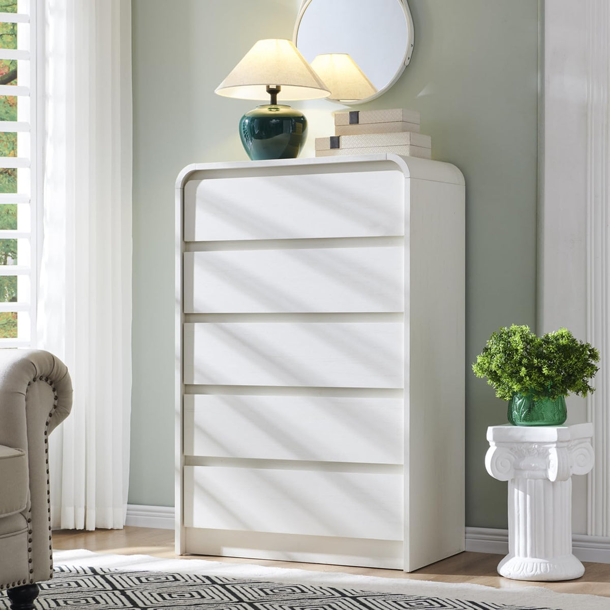 White tall chest beside a window with a lamp and mirror on top, sunlight creating diagonal bands across drawers.