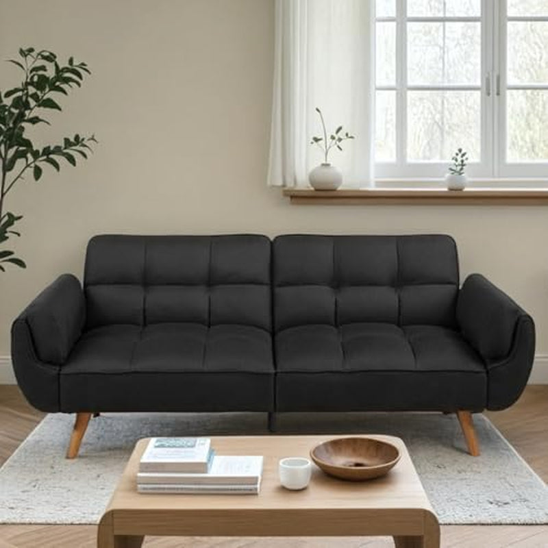 Charcoal futon sofa with tufted cushions and tapered wooden legs against a windowed wall.