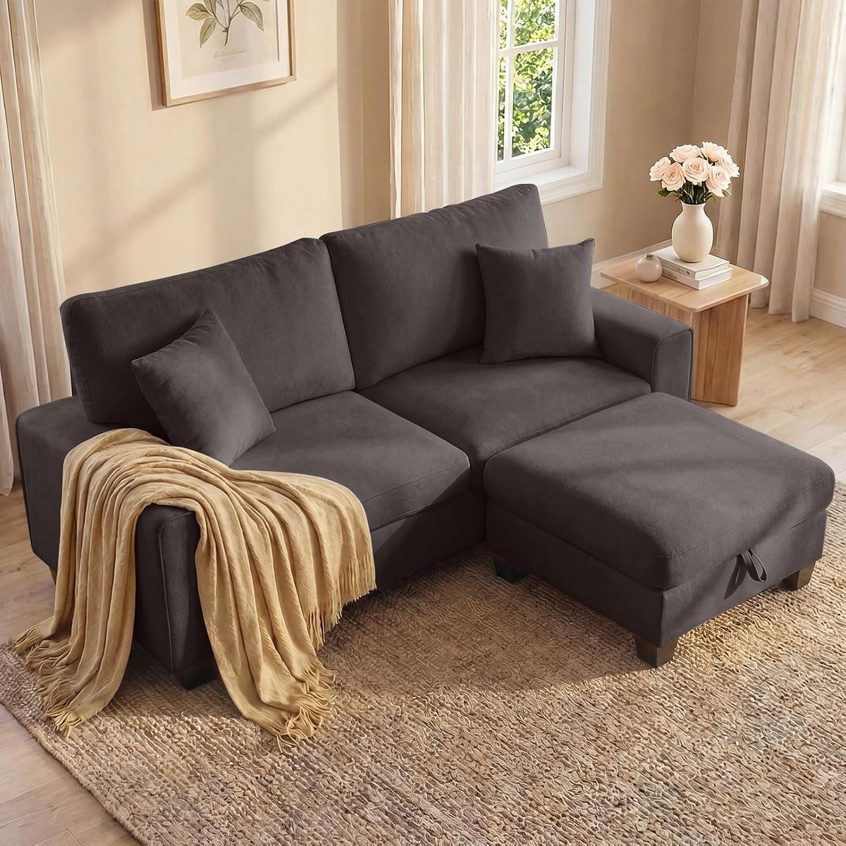 Dark charcoal loveseat with matching ottoman chaise in a sunlit corner, throw draped over armrest.