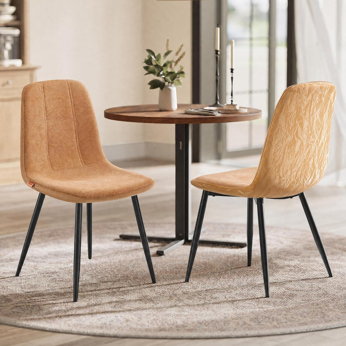 Two camel-tan chairs facing each other beside a small round wood bistro table on a round rug