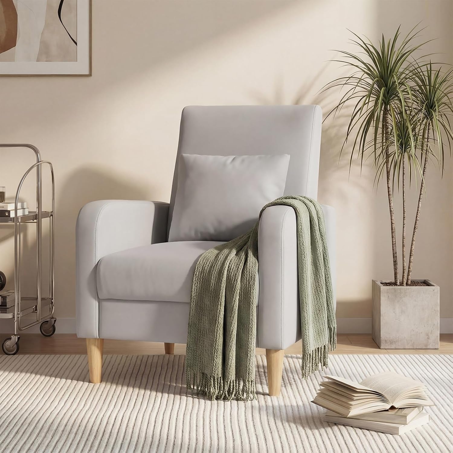 Single light gray fabric armchair with wooden legs, pillow and green throw draped over one arm