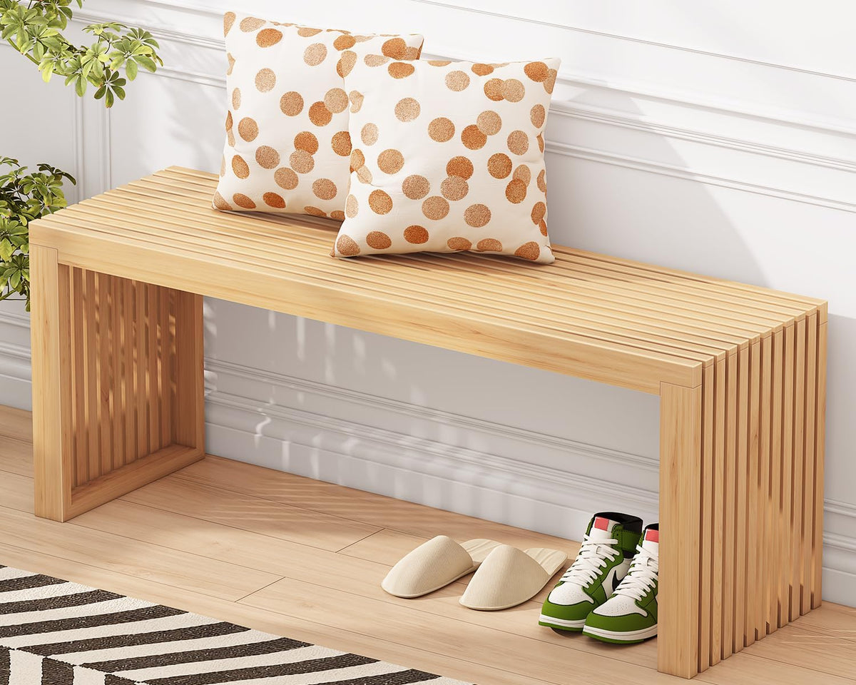 Natural bamboo bench with two patterned pillows against a white wall and slippers and shoes underneath