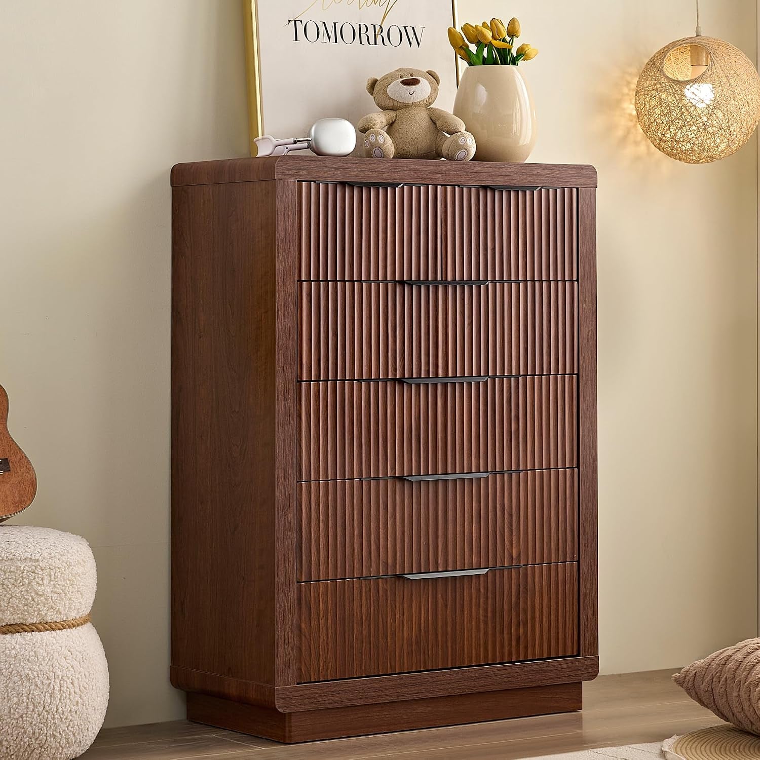 Tall walnut chest with vertically ribbed drawer fronts, black recessed handles and decorative items on top.