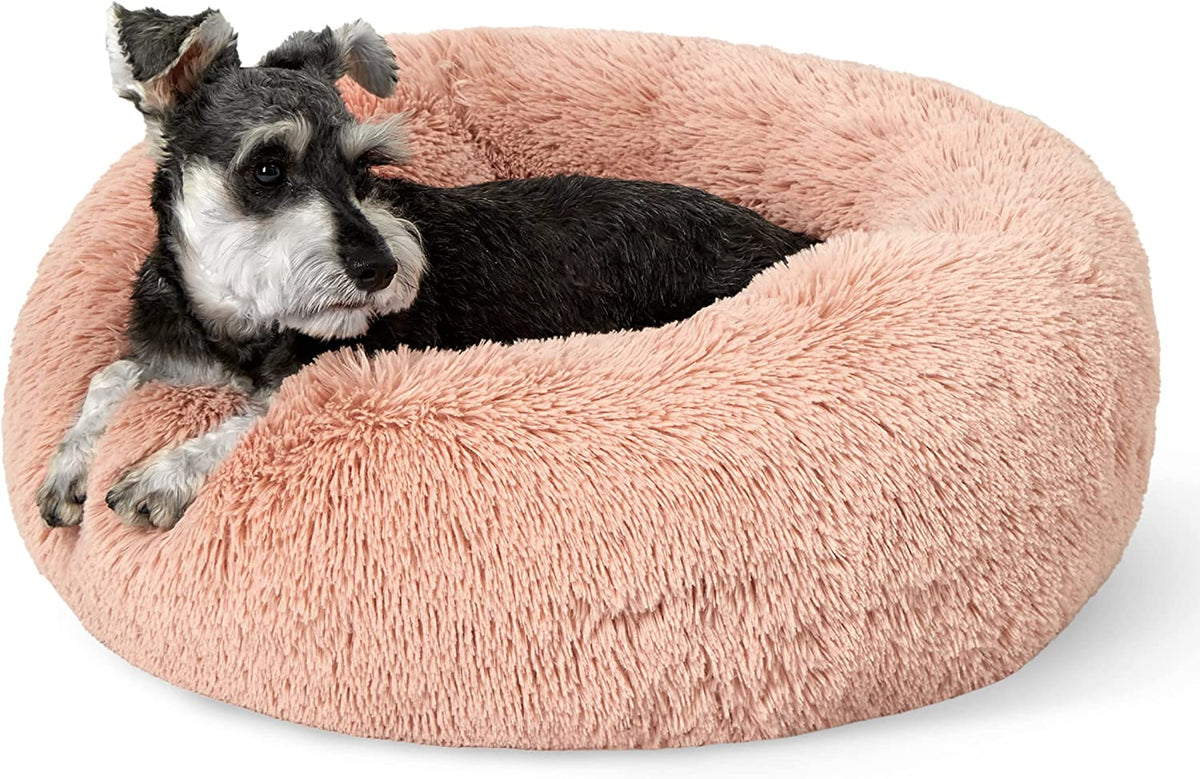 Blush pink round faux-fur donut bed with a small black-and-white dog resting inside.