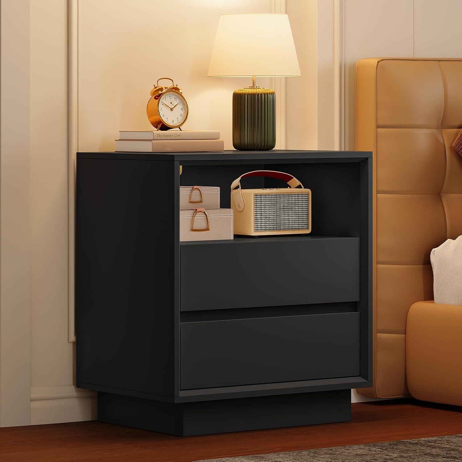 Black nightstand next to a bed showing open shelf and two drawer fronts in a warm bedroom setting