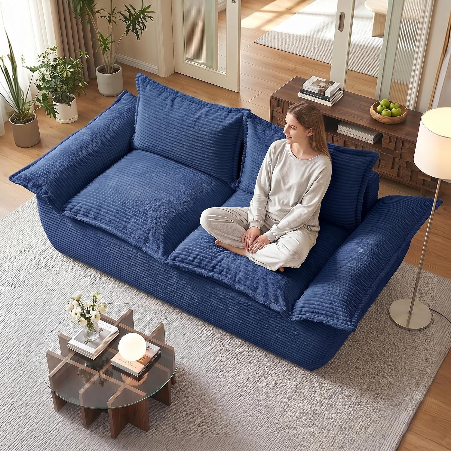 Overhead view of a deep blue corduroy two-seater sofa in a living room with a woman sitting cross-legged