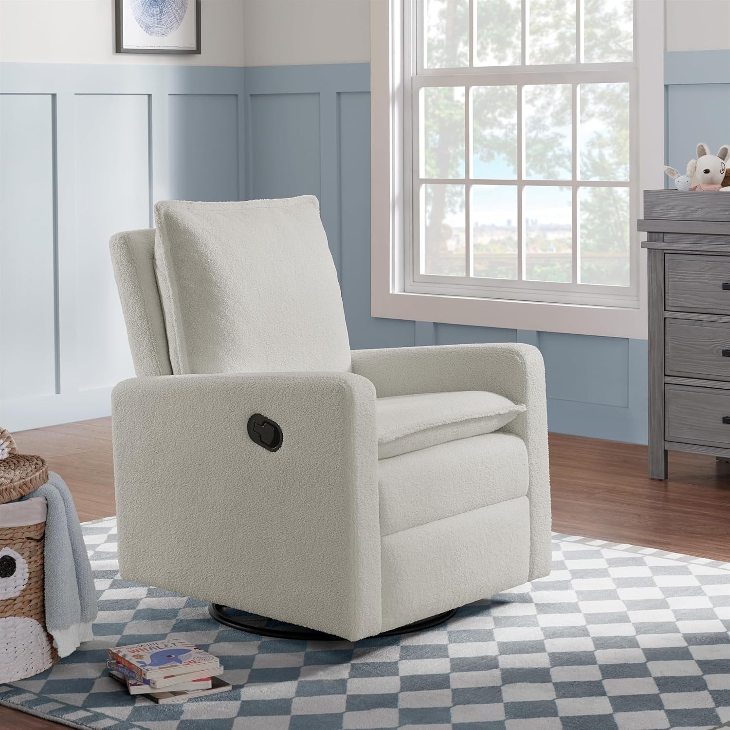 White boucle swivel glider placed in a nursery beside a window on a patterned rug.